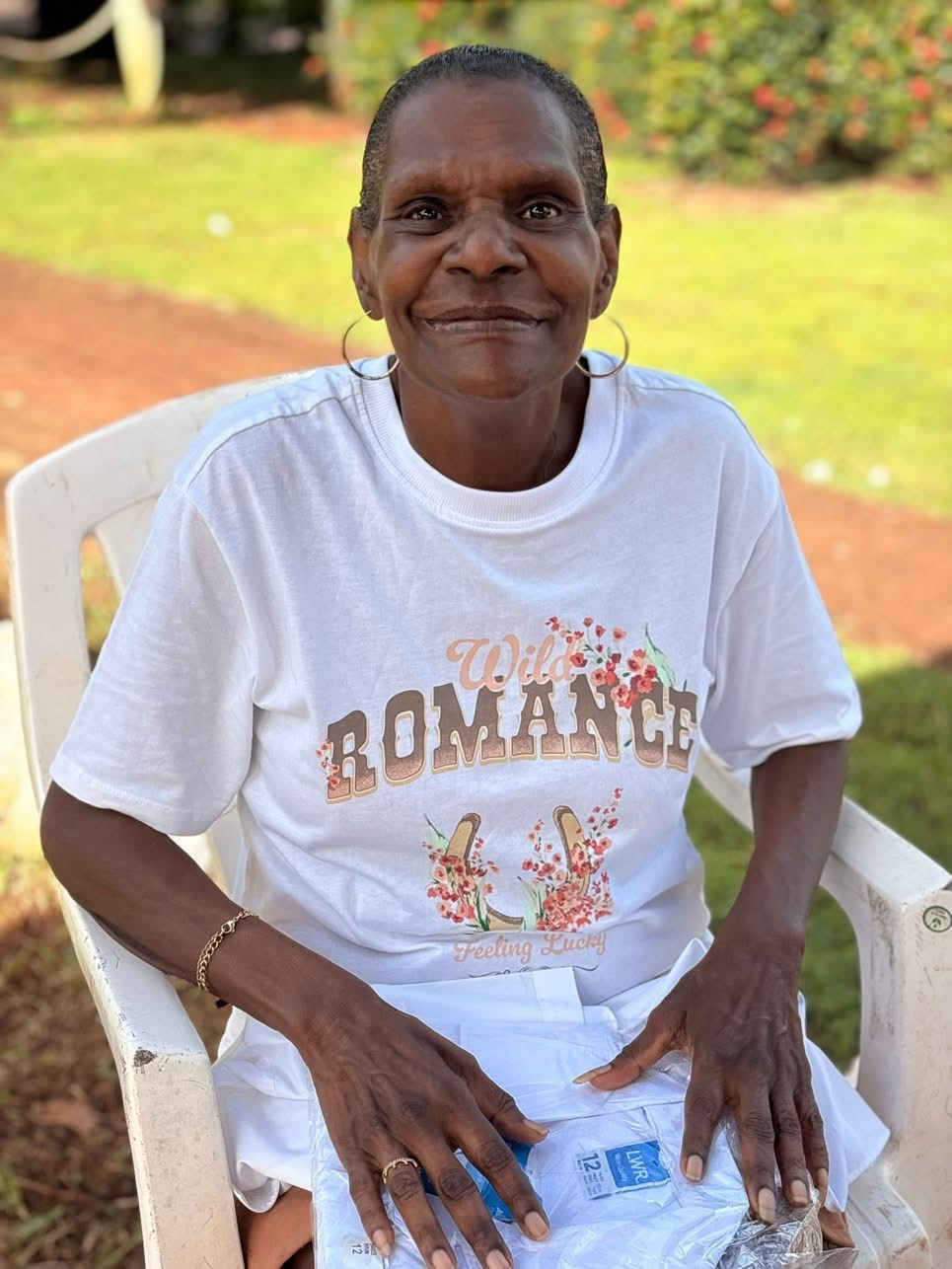 A woman seated outdoors in a white T-shirt