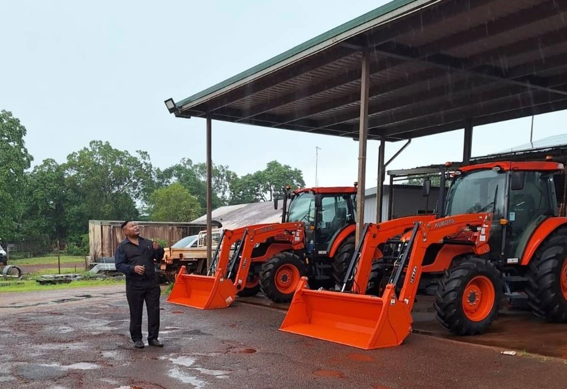 A person standing beside two orange tractors under a shelter