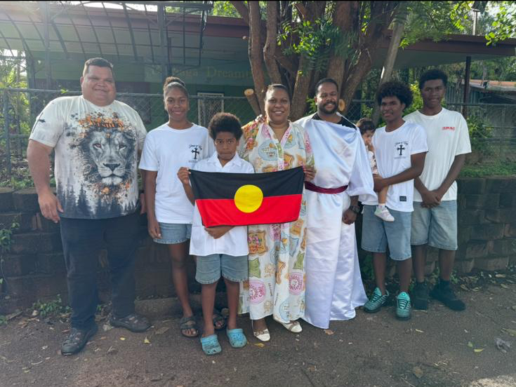Kingdom Kids children and adults gathered together outdoors with the Australian Aboriginal flag.